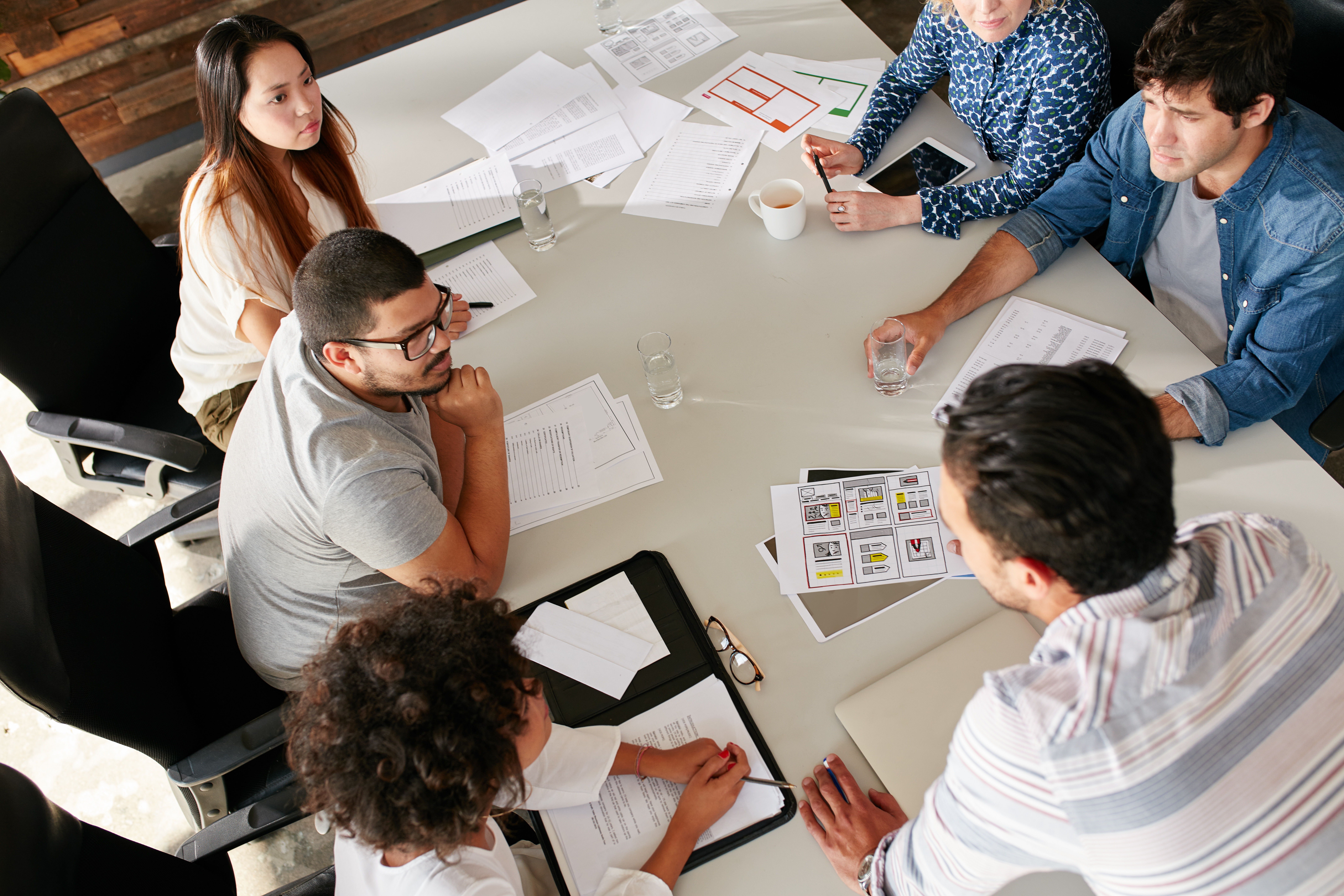 Team of creative professionals meeting in conference room High angle view of creative team sitting around table discussing business ideas. Mixed race team of creative professionals meeting in conference room.