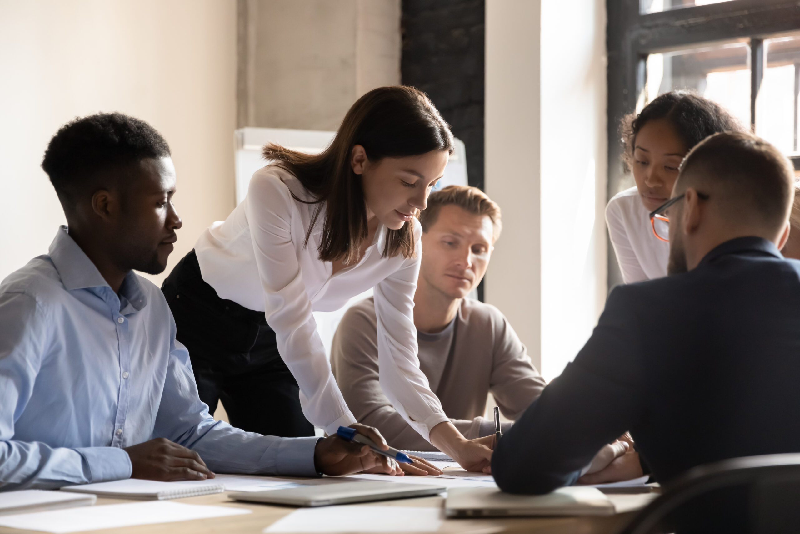 Diverse colleagues working on project together, sitting at table Diverse colleagues working on project together, sitting at table in boardroom, working with legal documents, financial report with statistics, employees engaged in teamwork at corporate meeting